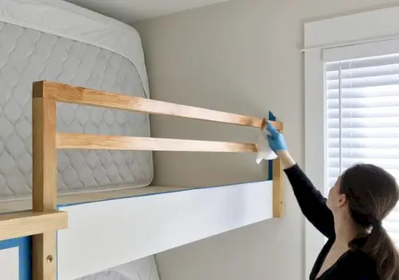 Sherry brengt beits aan op de railing van het stapelbed voor een ruwe houtlook
