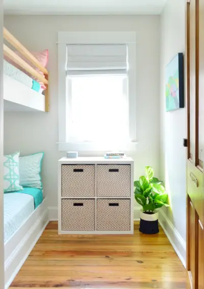 Kijk naar de stapelbedden in een kleine kamer met opbergmanden onder het raam