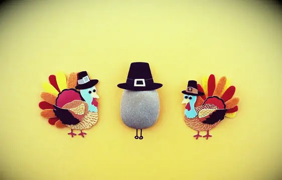 Felt cutouts of turkeys and a felt pilgrim hat atop a small stone