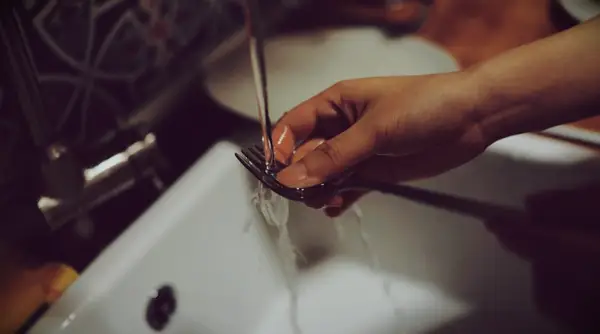 A hand washing a fork under running water.