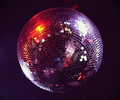 A shimmering disco ball hanging from a club ceiling. 