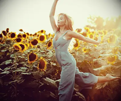 A blonde woman dancing in a field of sunflowers.