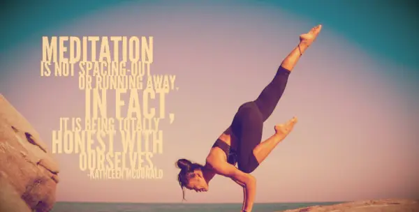 A woman in black doing a flying crow yoga pose against a blue desert sky