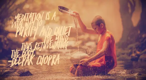 A young buddhist boy in orange sits in a pool, pouring water from a bowl onto a stone